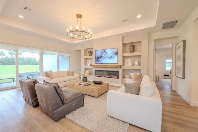 living area featuring light wood finished floors, built in shelves, visible vents, and a tray ceiling