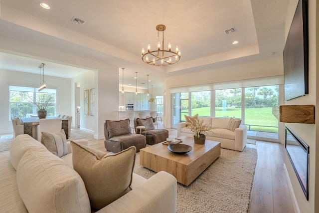 living room with a tray ceiling, light wood-type flooring, visible vents, and a notable chandelier