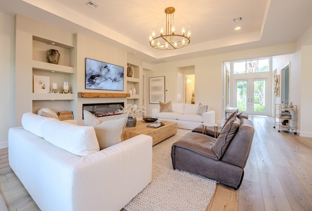 living room featuring built in shelves, a raised ceiling, and light wood-style floors