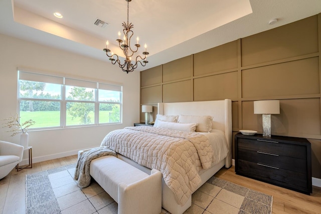 bedroom with light wood-type flooring, an inviting chandelier, and a tray ceiling