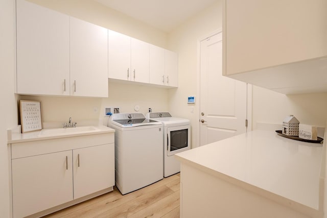 clothes washing area with light wood-type flooring, cabinet space, a sink, and washing machine and clothes dryer