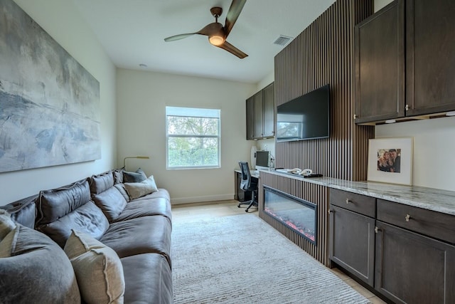 living area featuring a ceiling fan, visible vents, baseboards, and built in desk