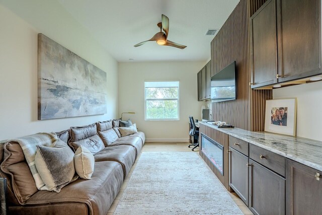 living room with light wood-type flooring, visible vents, ceiling fan, and baseboards