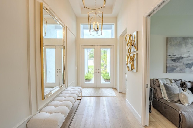 entryway with french doors, a notable chandelier, a towering ceiling, light wood-style floors, and baseboards