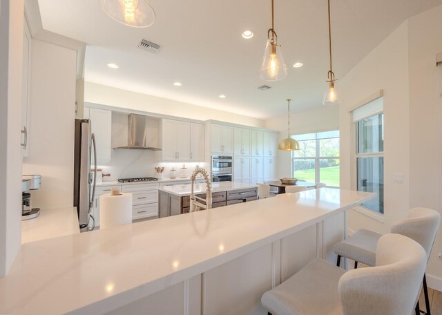 kitchen with visible vents, stainless steel appliances, light countertops, wall chimney range hood, and a kitchen bar