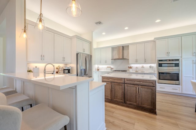 kitchen featuring visible vents, wall chimney exhaust hood, appliances with stainless steel finishes, a breakfast bar area, and light countertops