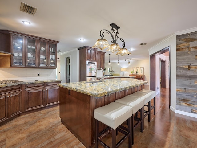 kitchen with a breakfast bar area, a sink, visible vents, ornamental molding, and decorative backsplash