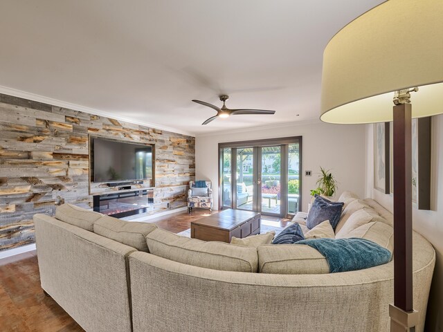 living room with a ceiling fan, an accent wall, ornamental molding, wood finished floors, and french doors