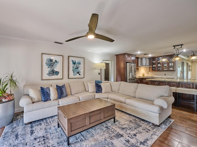 living room with a ceiling fan, visible vents, crown molding, and wood finished floors