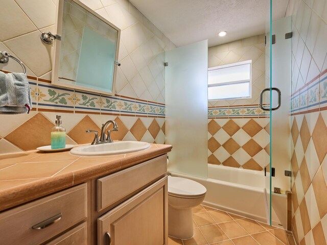 full bath with toilet, shower / bath combination with glass door, vanity, tile walls, and tile patterned floors