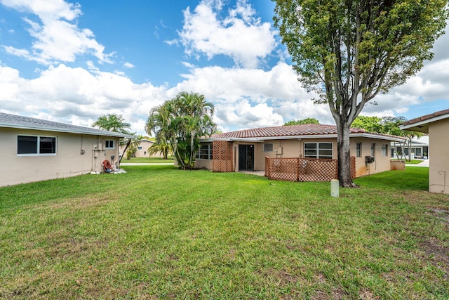 rear view of property featuring a tile roof, a lawn, and stucco siding