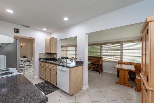 kitchen featuring light tile patterned floors, visible vents, white dishwasher, light brown cabinets, and a sink