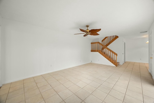 spare room featuring ceiling fan, light tile patterned flooring, visible vents, baseboards, and stairway