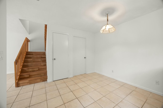 spare room featuring light tile patterned floors, baseboards, and stairway