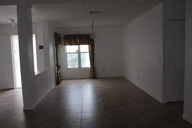 tiled empty room with baseboards and a textured ceiling