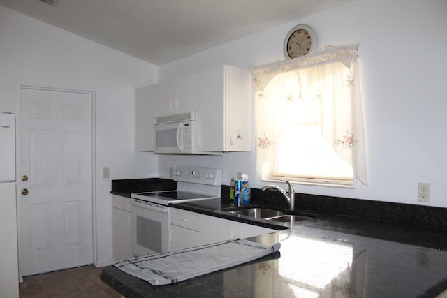 kitchen featuring dark countertops, white cabinetry, a sink, white appliances, and tile patterned floors