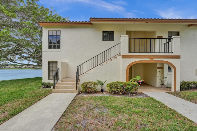 view of front of home with a water view, stairs, a front yard, stucco siding, and a balcony