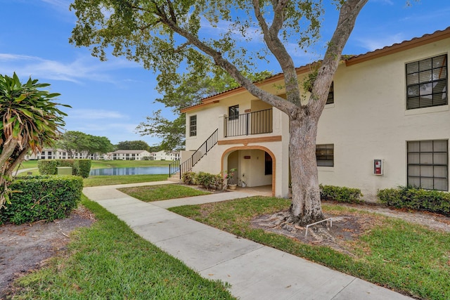 view of front of property featuring stucco siding, a water view, stairs, and a tiled roof