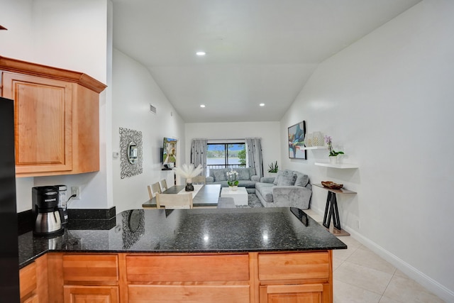 kitchen featuring dark stone countertops, light tile patterned floors, a peninsula, and vaulted ceiling