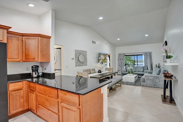 kitchen with dark stone countertops, a peninsula, freestanding refrigerator, and high vaulted ceiling