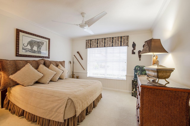 bedroom with a wainscoted wall, ornamental molding, a ceiling fan, and light colored carpet