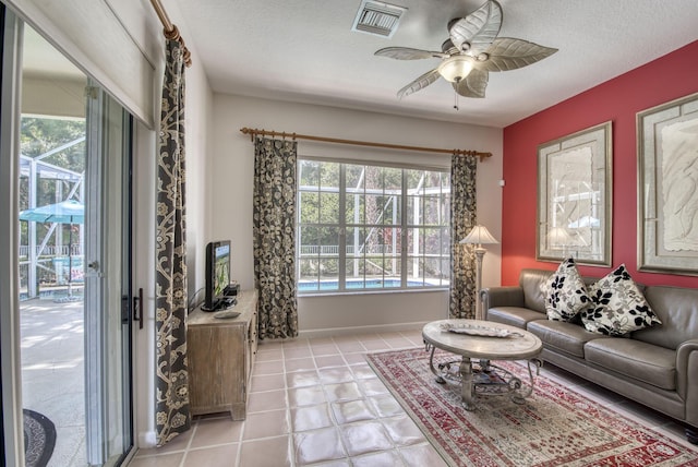 living room featuring baseboards, ceiling fan, visible vents, and a textured ceiling