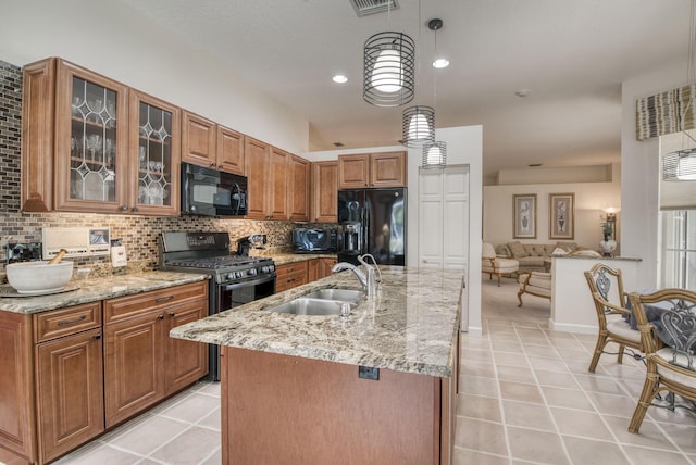 kitchen with a sink, decorative backsplash, brown cabinets, black appliances, and a center island with sink