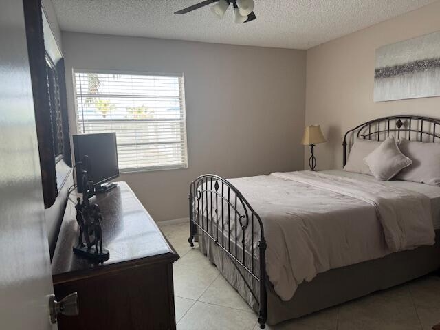 bedroom with a textured ceiling, light tile patterned flooring, a ceiling fan, and baseboards