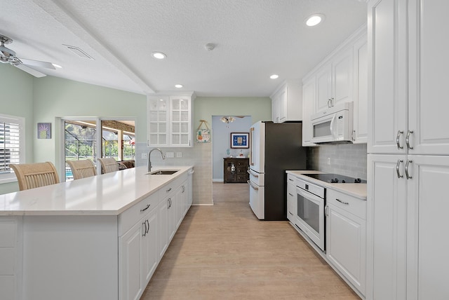 kitchen featuring light wood-type flooring, a sink, backsplash, white appliances, and a peninsula