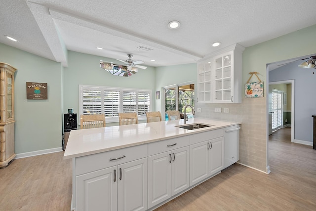 kitchen with a ceiling fan, a sink, light wood-style floors, a peninsula, and dishwasher