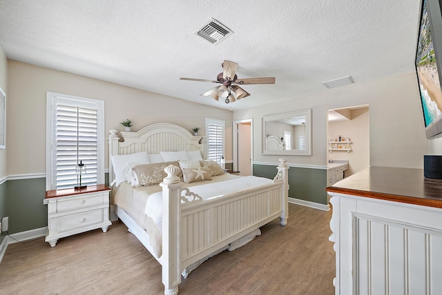 bedroom featuring a ceiling fan, baseboards, visible vents, a textured ceiling, and light wood-type flooring