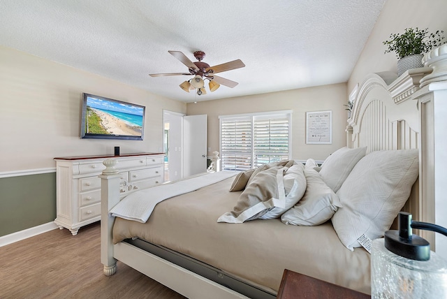 bedroom featuring baseboards, a textured ceiling, ceiling fan, and light wood finished floors