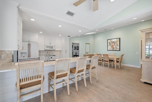 kitchen featuring white appliances, visible vents, lofted ceiling, a sink, and a kitchen breakfast bar