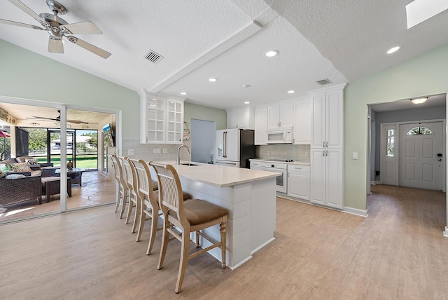 kitchen featuring visible vents, white appliances, a peninsula, a breakfast bar area, and lofted ceiling