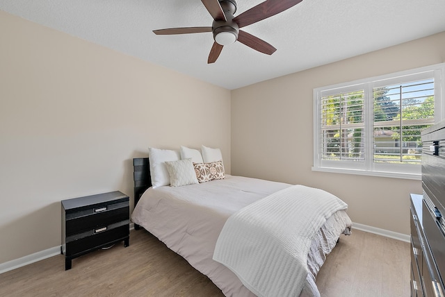 bedroom with a textured ceiling, light wood-style flooring, baseboards, and ceiling fan