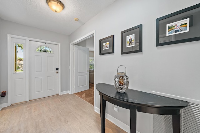 foyer entrance featuring light wood-style flooring, baseboards, and a textured ceiling