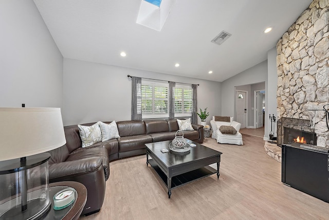 living room featuring light wood-type flooring, visible vents, lofted ceiling with skylight, and a stone fireplace