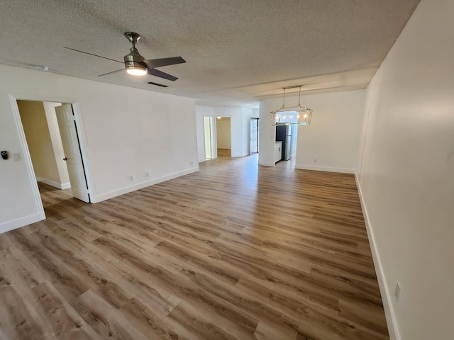 interior space featuring a textured ceiling, ceiling fan with notable chandelier, wood finished floors, visible vents, and baseboards