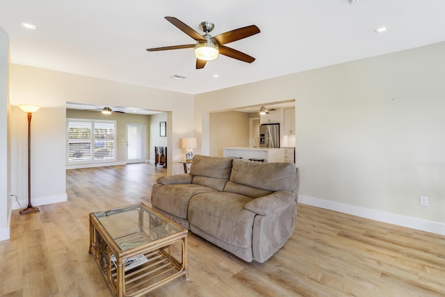 living room with light wood finished floors, visible vents, baseboards, and a ceiling fan