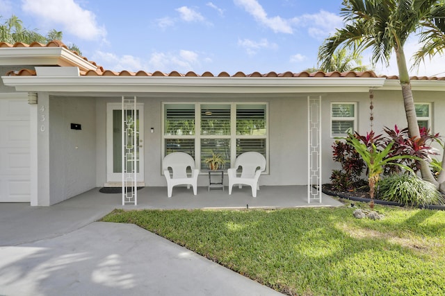 view of exterior entry with a porch, a lawn, and stucco siding