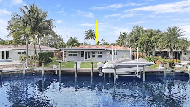 rear view of house with a water view, boat lift, a tile roof, and a lawn