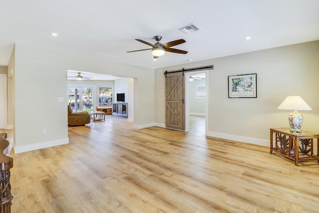 living room featuring a barn door, baseboards, visible vents, ceiling fan, and wood finished floors