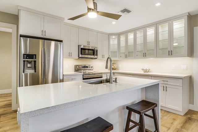 kitchen featuring visible vents, a breakfast bar, stainless steel appliances, light wood-type flooring, and a sink