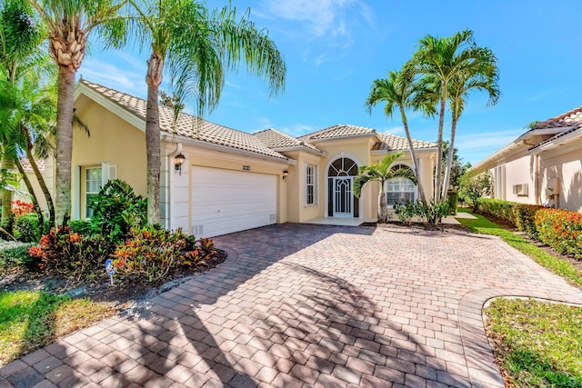 mediterranean / spanish house featuring a garage, a tiled roof, decorative driveway, and stucco siding