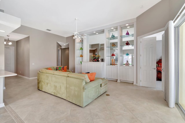 living area featuring light tile patterned floors, baseboards, built in features, and ceiling fan with notable chandelier