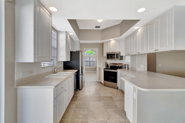 kitchen with appliances with stainless steel finishes, light countertops, white cabinetry, and backsplash