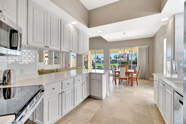 kitchen with appliances with stainless steel finishes, white cabinets, a peninsula, and tasteful backsplash