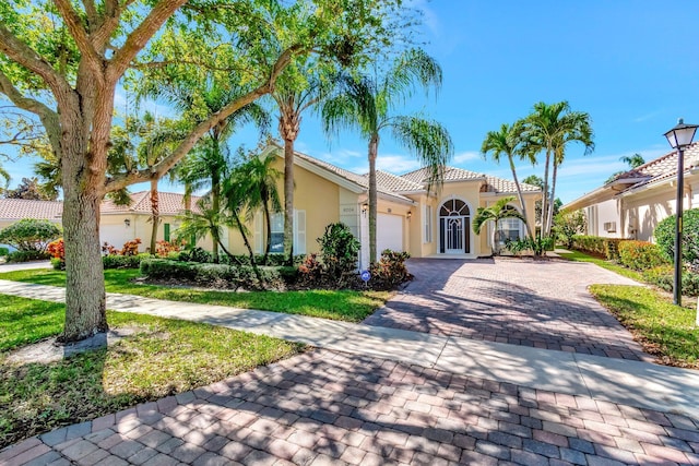 mediterranean / spanish-style home featuring an attached garage, a tiled roof, decorative driveway, and stucco siding