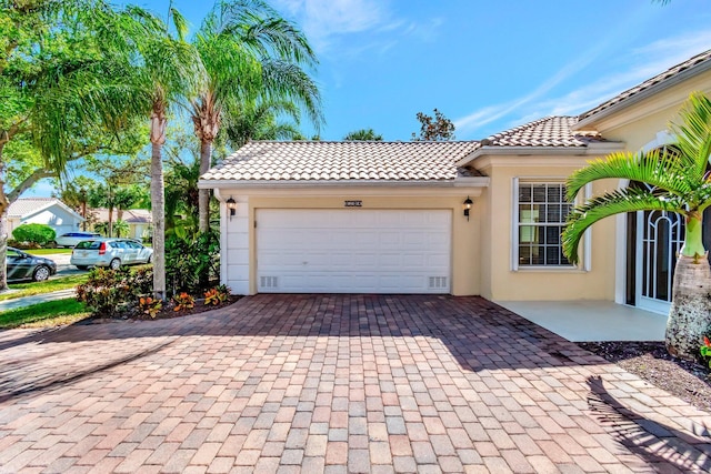 view of front of home with decorative driveway, a tile roof, an attached garage, and stucco siding