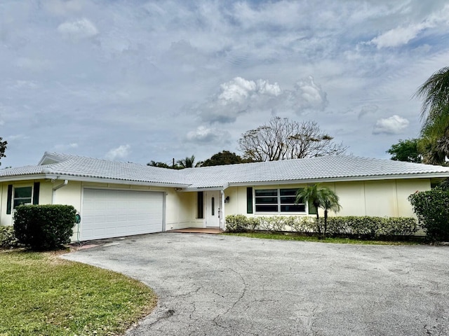 single story home featuring driveway, a tiled roof, an attached garage, and stucco siding